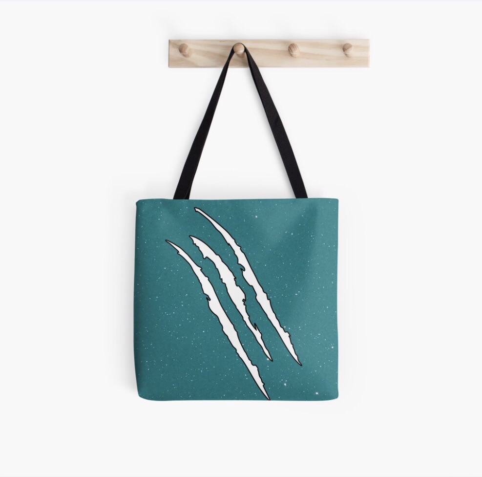 A teal tote bag featuring claw mark designs in white, hanging on a wooden peg.