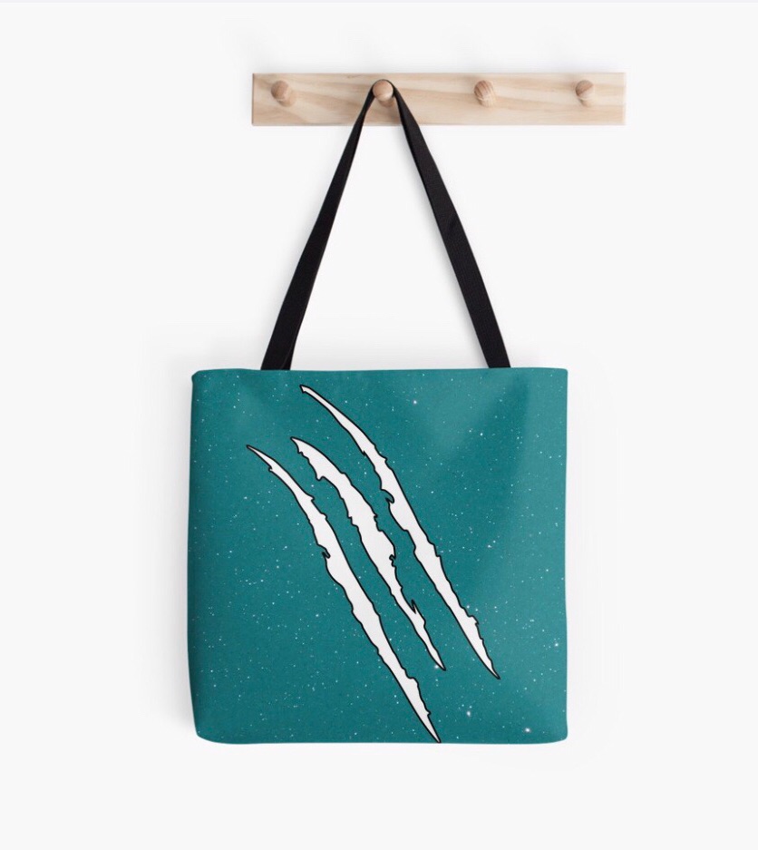 Teal tote bag with claw marks design hanging on a wooden hook.